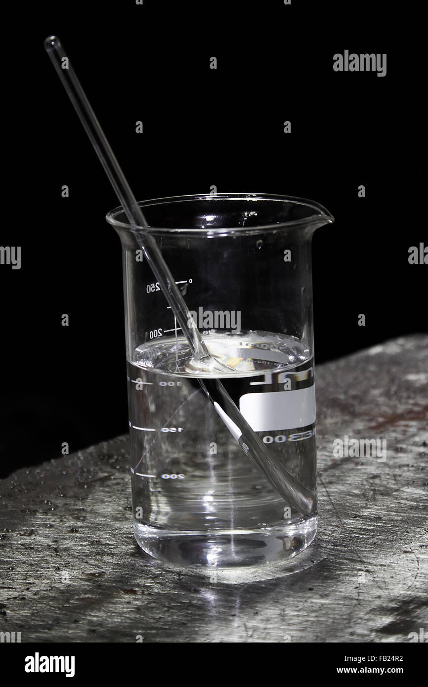 Bacchetta di vetro seduta nel bicchiere di vetro riempito con acido nitrico per metallo macro test di attacco Foto Stock