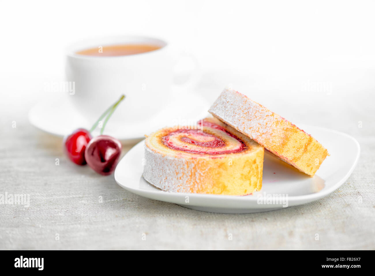 Rotolo con ciliegie sulla piastra e cappuccio di tè, close up Foto Stock