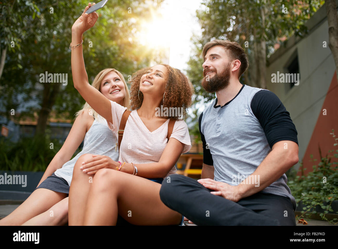 Tre giovani amici prendendo un selfie con cellulare. Gruppo multirazziale di giovani divertirsi insieme mentre seduti all'aperto Foto Stock