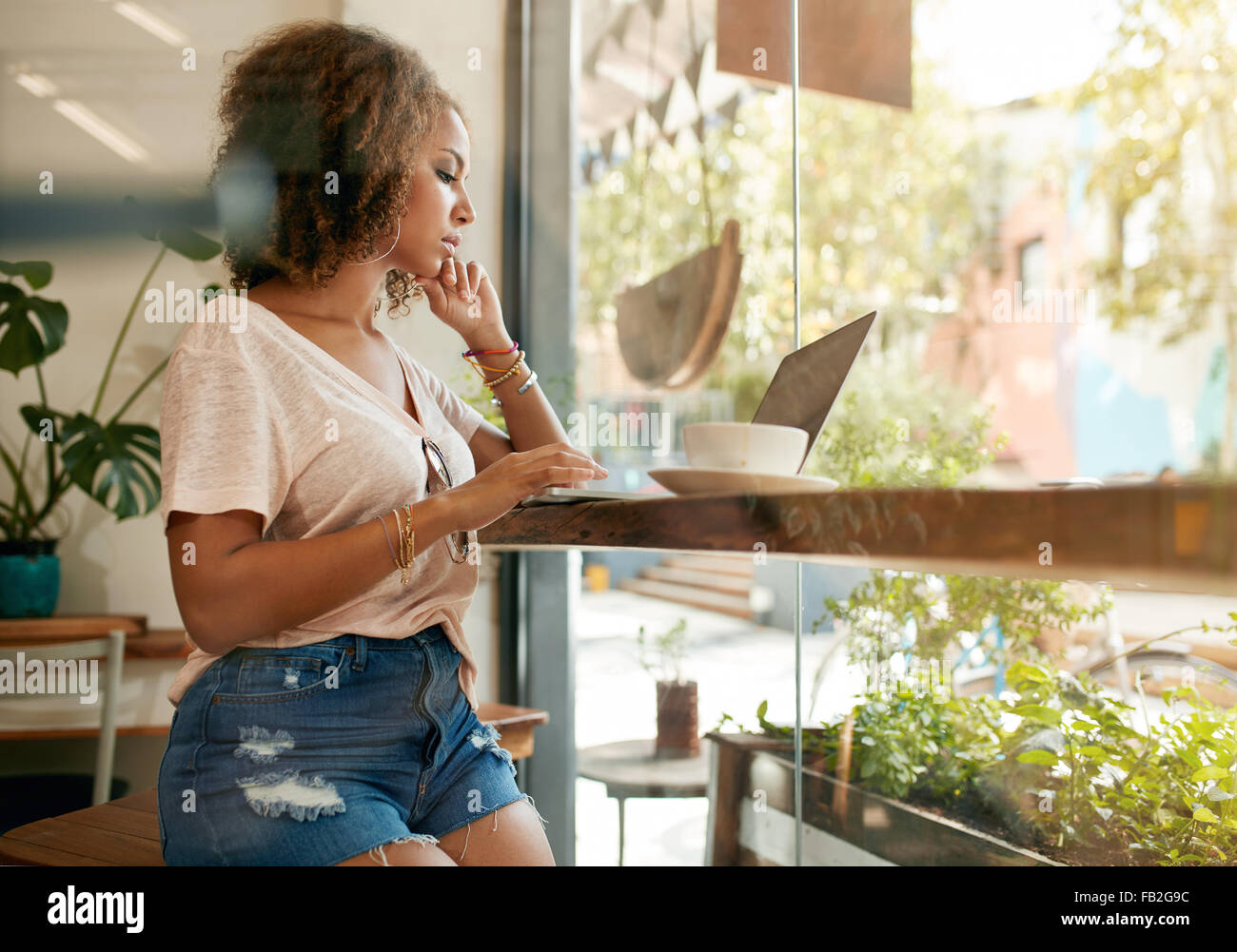 Colpo di una giovane donna che utilizza il suo computer portatile in una caffetteria. Femmina africana in seduta cafe navigando in internet sul suo computer portatile. Foto Stock