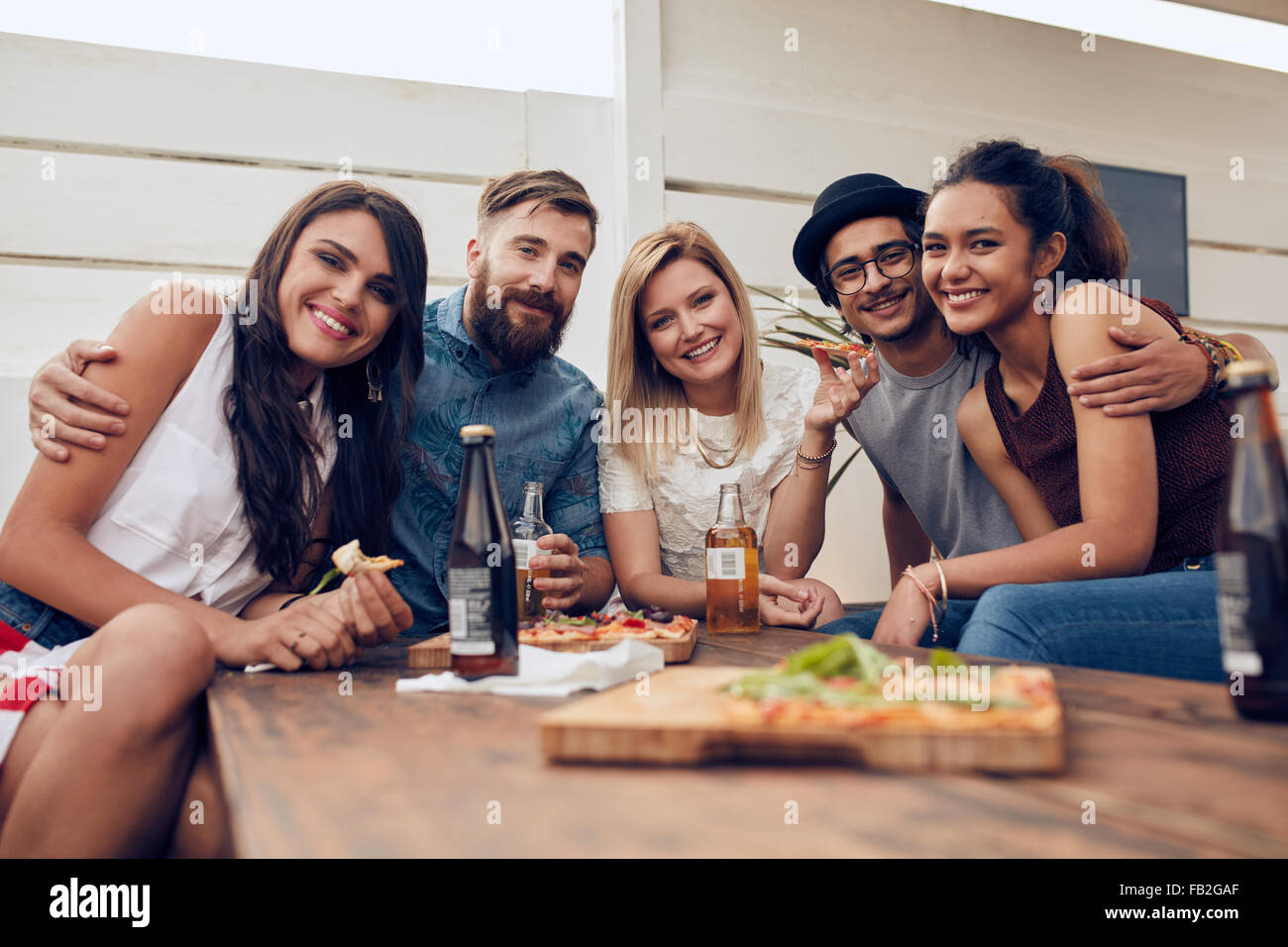 Gruppo di amici riuniti attorno al tavolo in corrispondenza di una parte del tetto. Multirazziale giovani guardando la fotocamera e sorridente. Foto Stock
