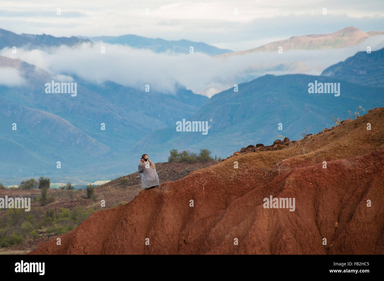 Donna seduta sulla grande pietra arenaria rossa rock formazione pendenza nel caldo secco del deserto di Tatacoa, Huila Foto Stock