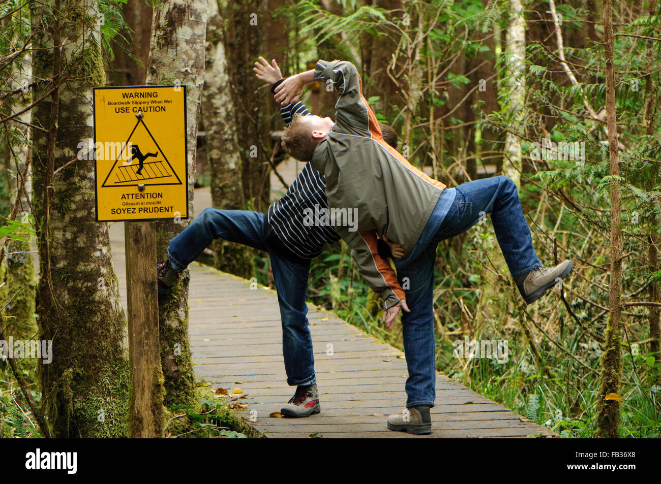 Due ragazzi scherzi circa un scivoloso quando è bagnato segno a una passerella in Pacific Rim National Park, BC, Canada Foto Stock