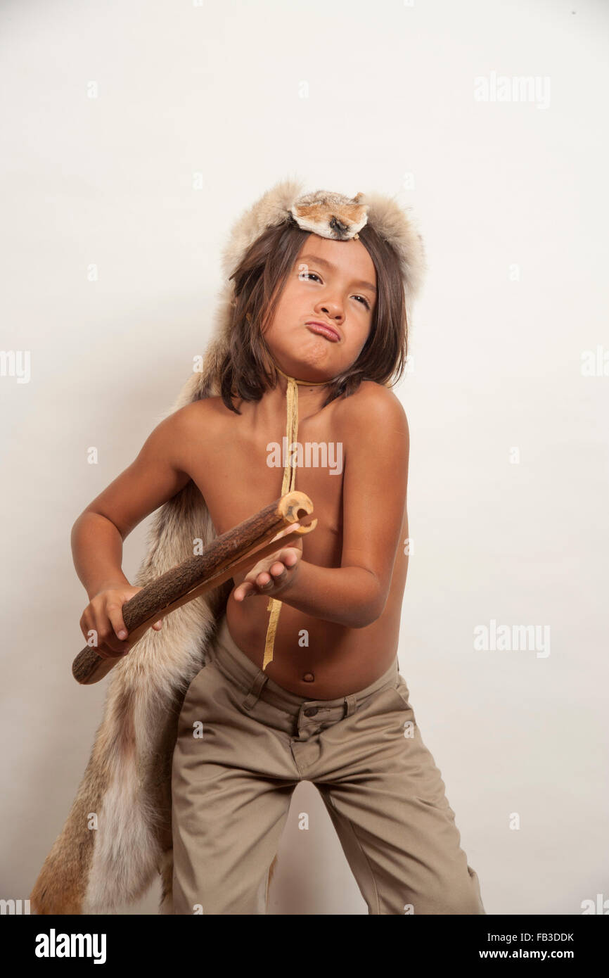 Un Native American boy membro della tribù Acjachemen riproduce il battaglio stick, una primitiva di percussioni di strumenti musicali. Nota testa di coyote costume appropriato per maschi membri tribali.Modello di Rilascio modello di rilascio Foto Stock