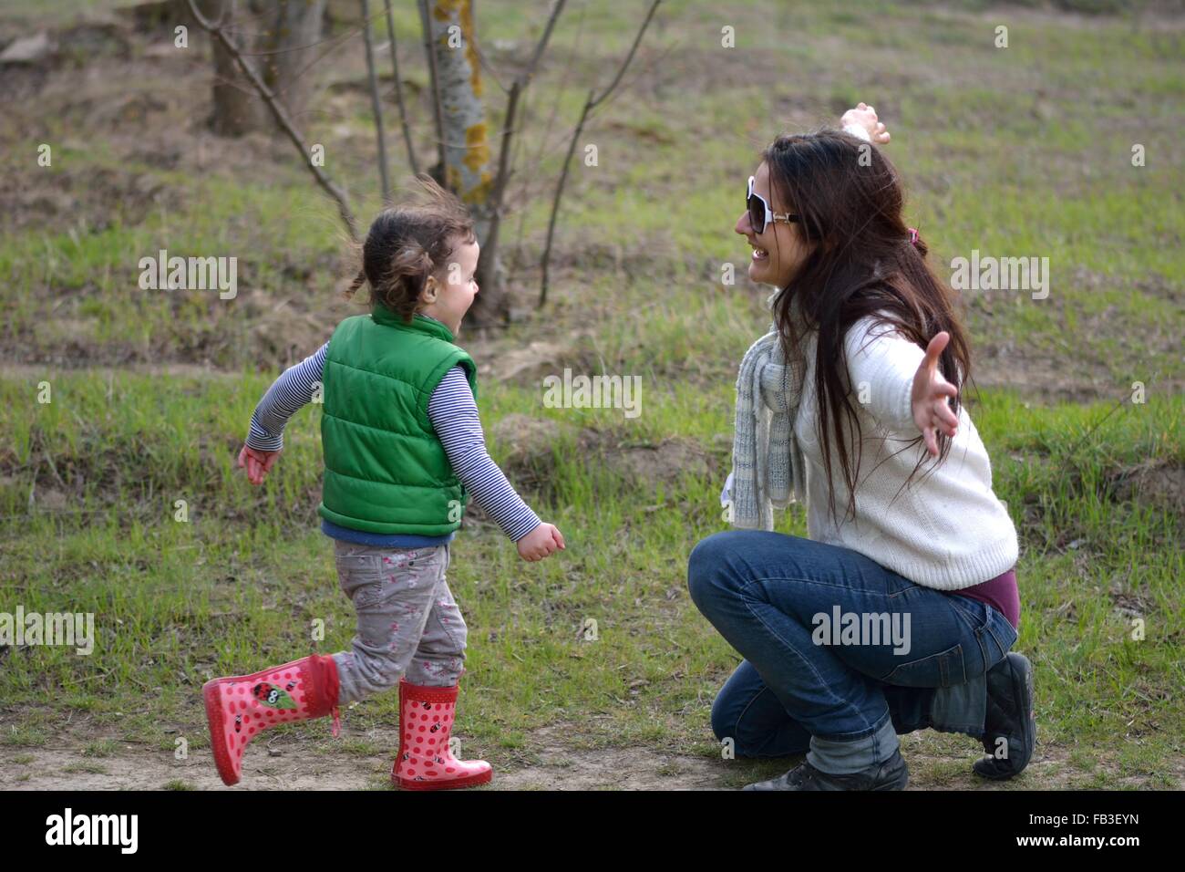 Ragazza giovane con pig-tail in esecuzione nella madre di braccia aperte. Un bambino sorridente sprint alla sua Madre in ginocchio, pronto per un abbraccio. Foto Stock