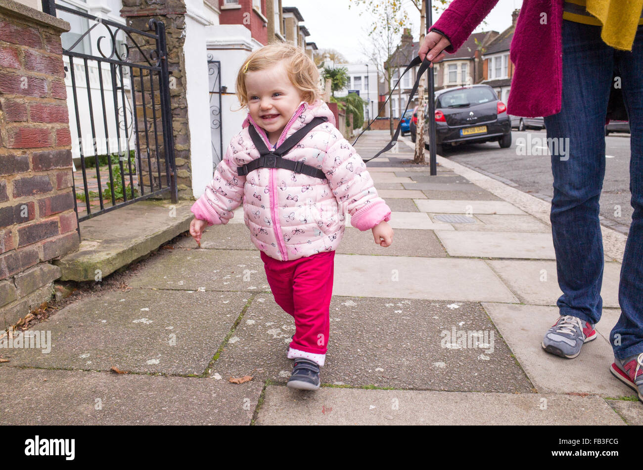 Il Toddler camminare per la strada tenuto con un cavo di sicurezza, London, Regno Unito Foto Stock