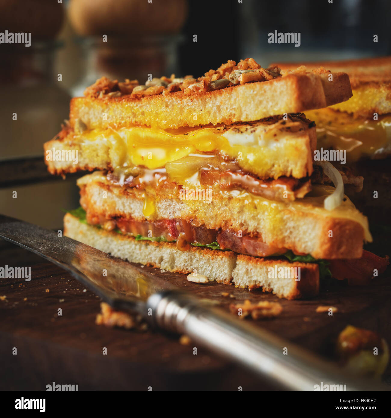 Sandwich con uova, pomodoro, cipolla e pancetta su un vintage sfondo in legno in stile rustico. Tonica. Foto Stock