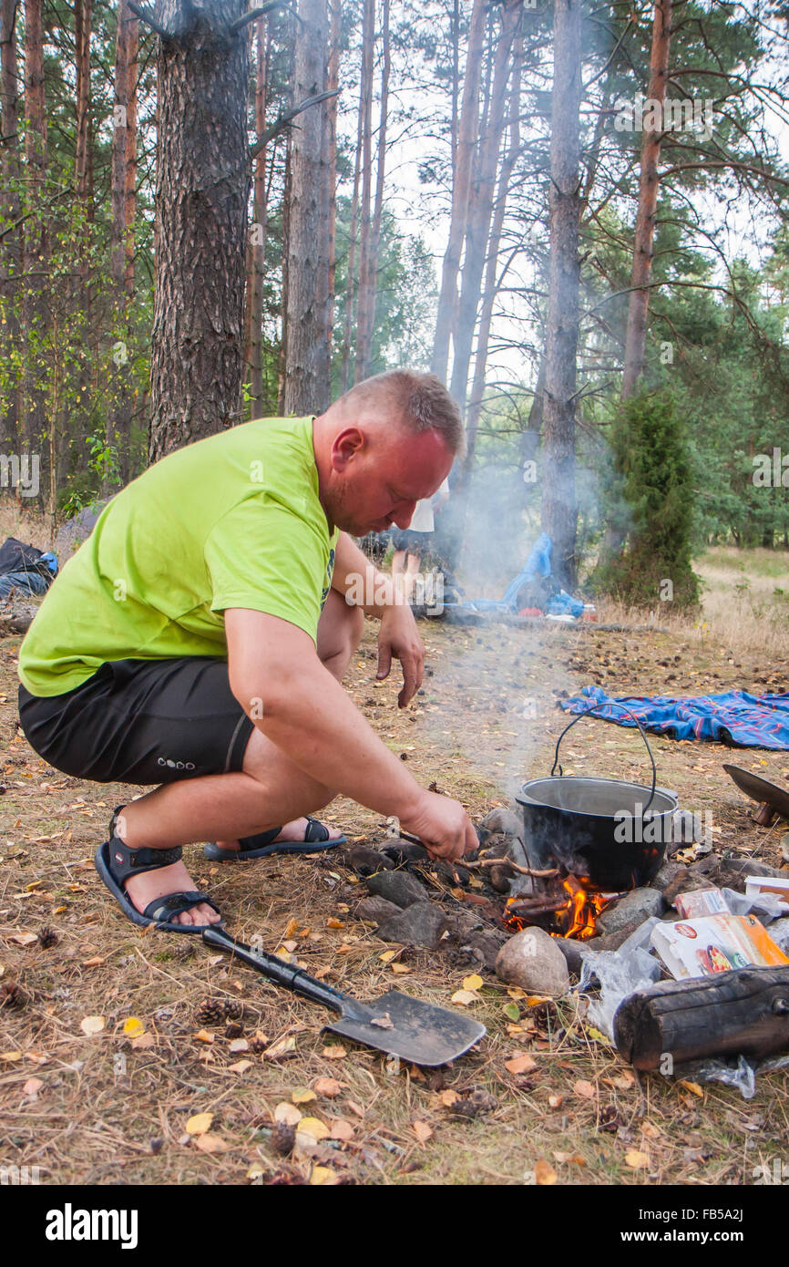 Fiume Pilawa, Polonia - 26 agosto 2015: un uomo accende un fuoco sotto un bollitore durante la cottura del pasto. Foto Stock