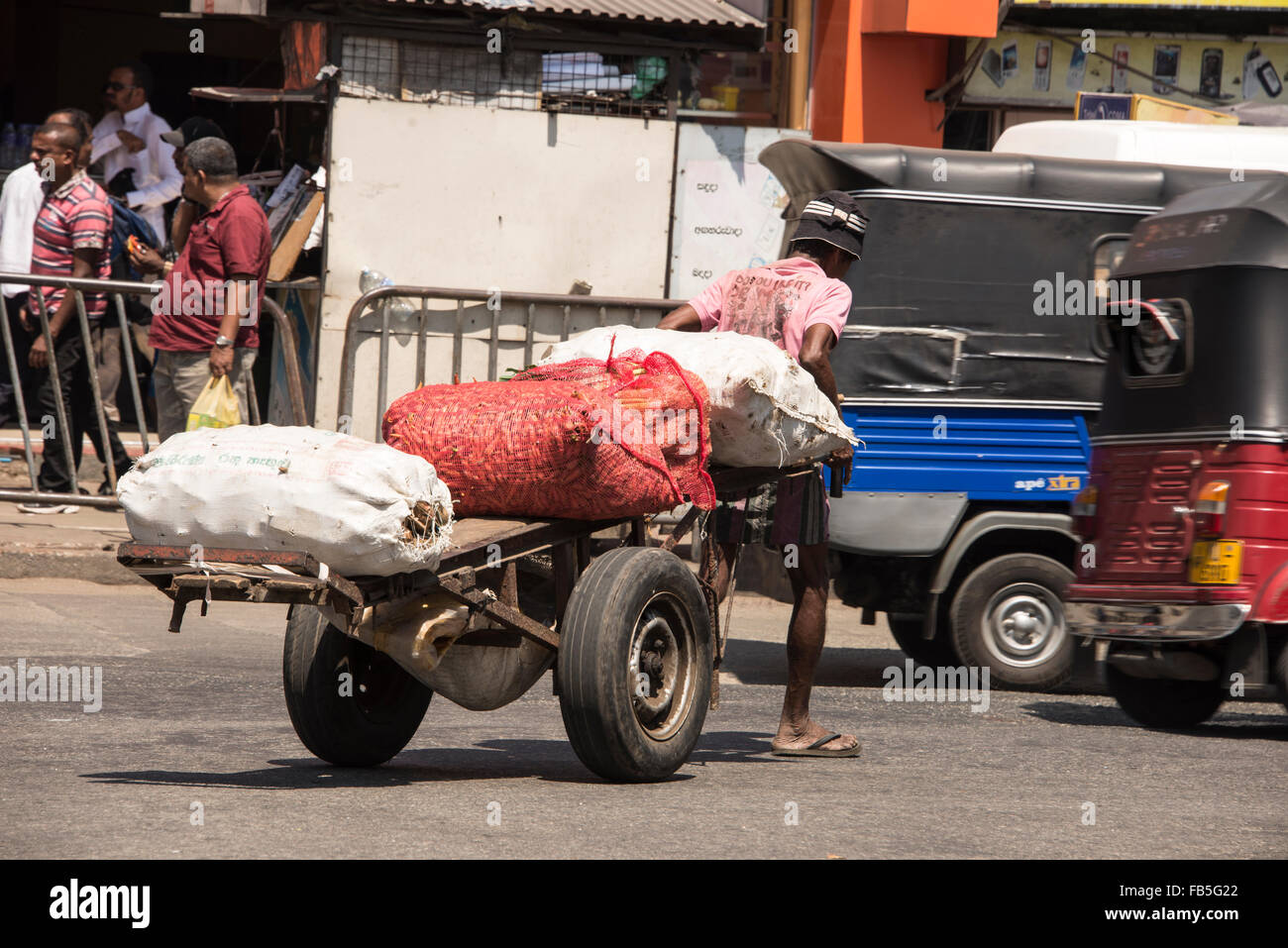Un mercato trader tirando il suo carrello di verdure lungo una strada trafficata in Pettah distretto di Colombo, Sri Lanka Foto Stock