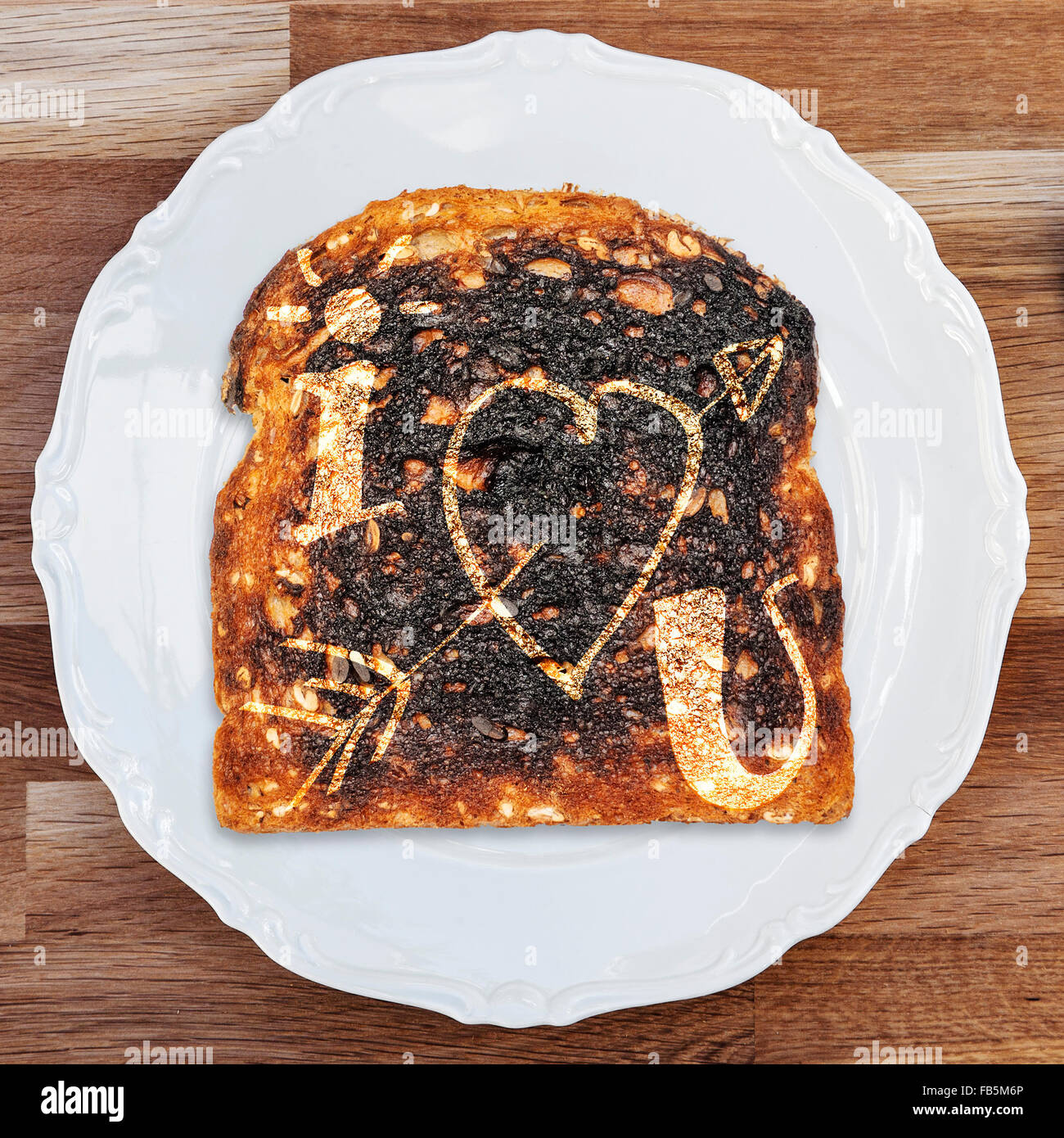 Una fetta di pane tostato bruciato con un I Love U messaggio su un bianco lucido piastra posta su di un tavolo di legno superficie. Foto Stock