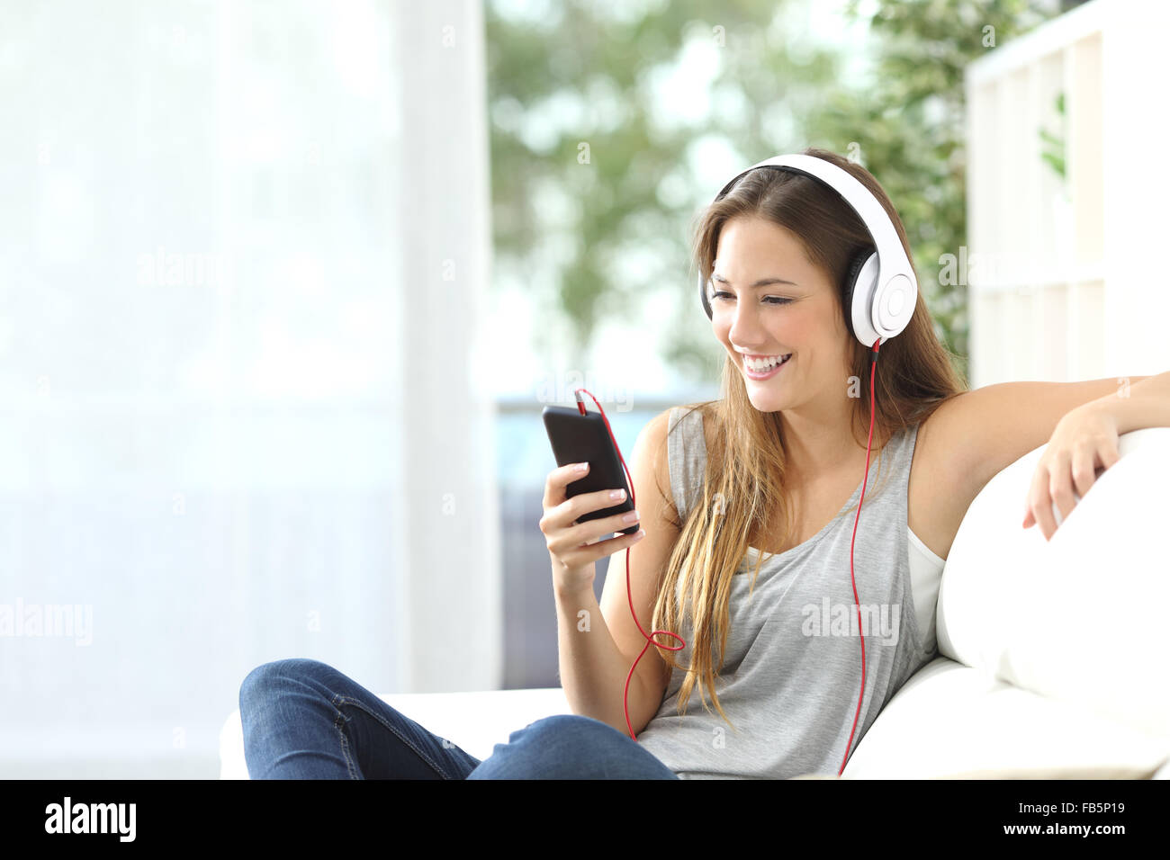 Happy girl ascoltare musica dal telefono cellulare seduti su un lettino a casa Foto Stock