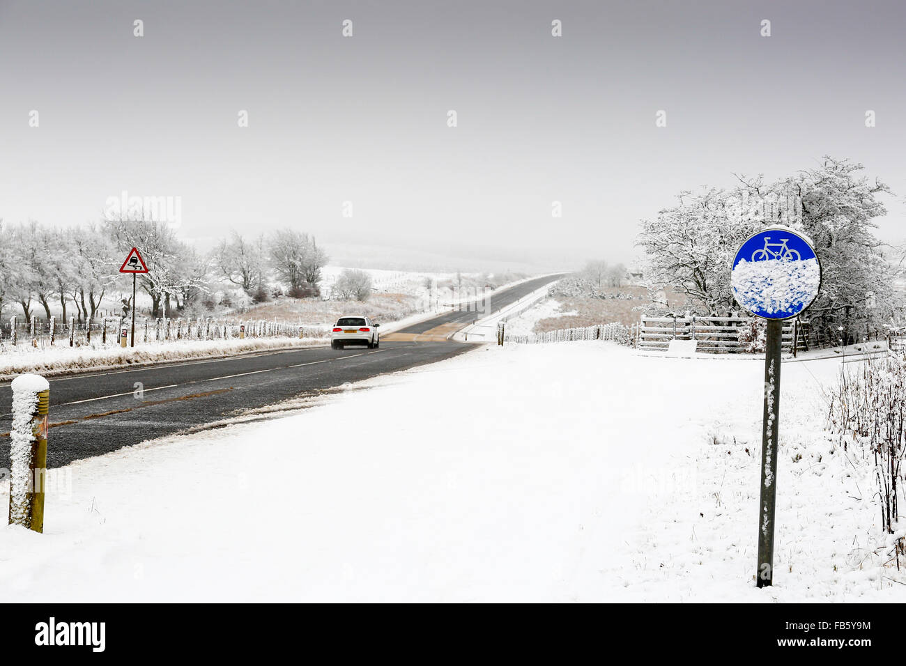 Veicolo in marcia su una strada di campagna in pericolose condizioni di innevamento, con la pista ciclabile coperto di neve, Ayrshire, in Scozia, Regno Unito Foto Stock