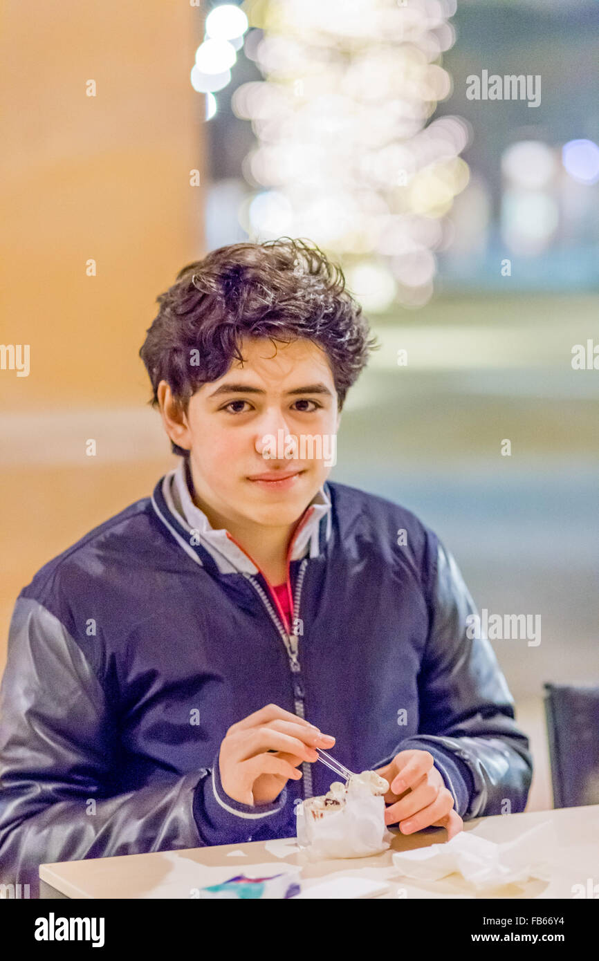 Chiudere il ritratto di ragazzo caucasico a mangiare il gelato in inverno con aspetto rassicurante nella calorosa e ambiente luminoso Foto Stock