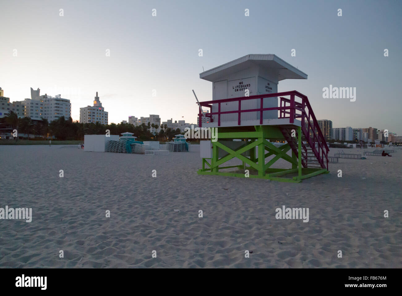 Al tramonto, una stazione bagnino sulla spiaggia sabbiosa con parzialmente illuminata South Beach hotel edifici in background , Miami Beach, Florida. Foto Stock