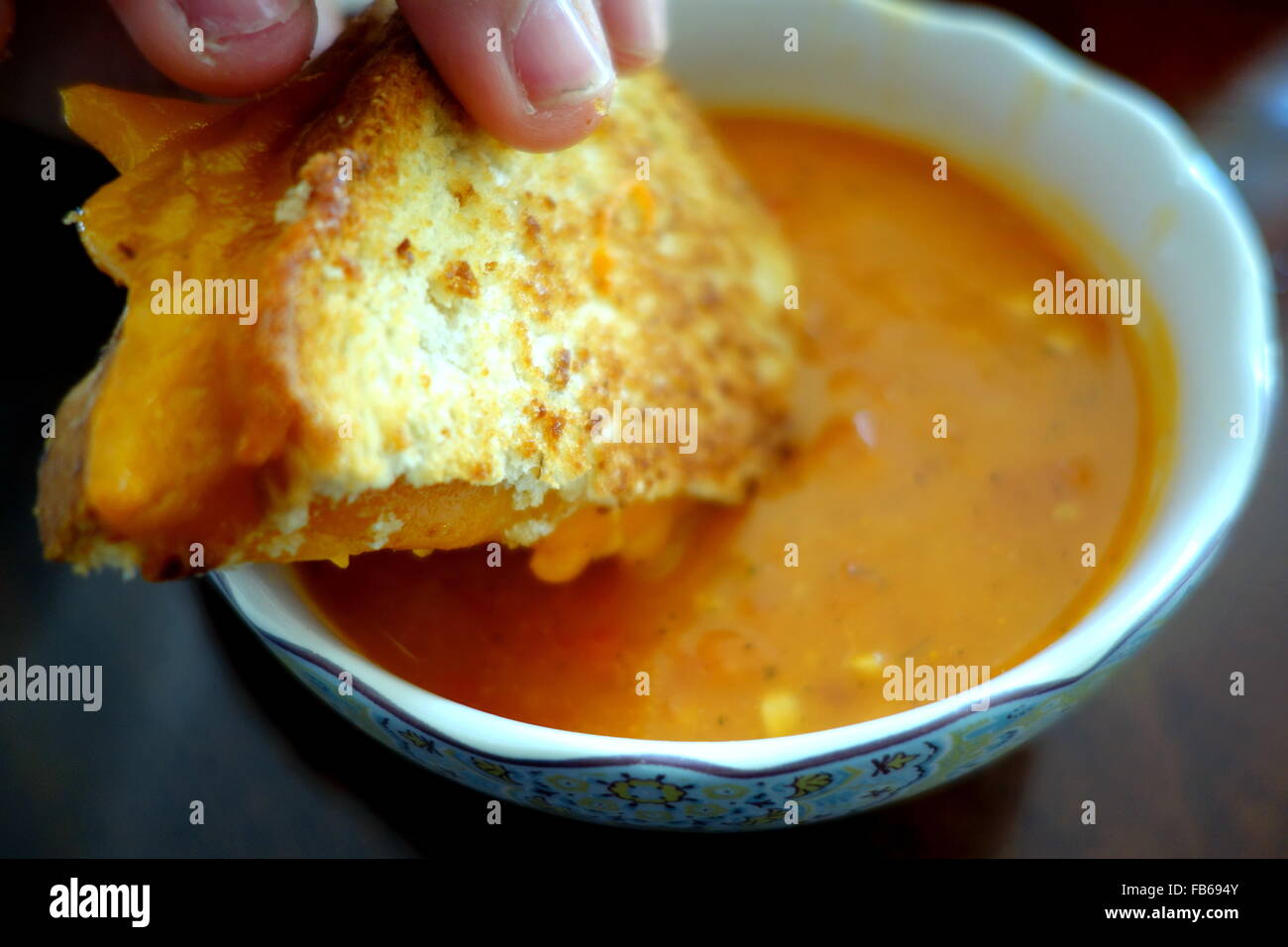 Mano che tiene un formaggio alla griglia panino immerso in una ciotola di cremosa zuppa di pomodoro Foto Stock