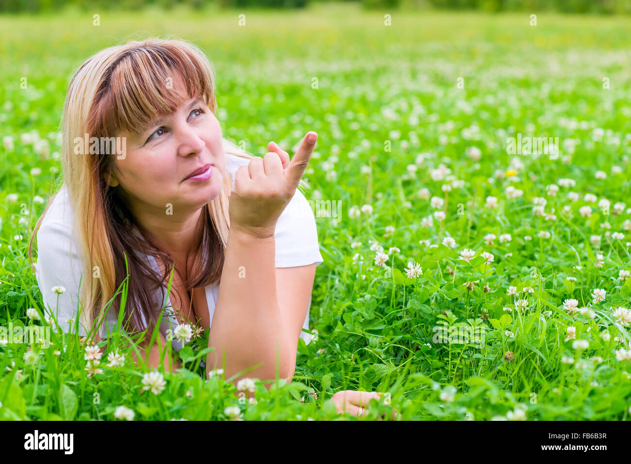 Donna matura su un prato verde che mostra un dito in direzione Foto Stock