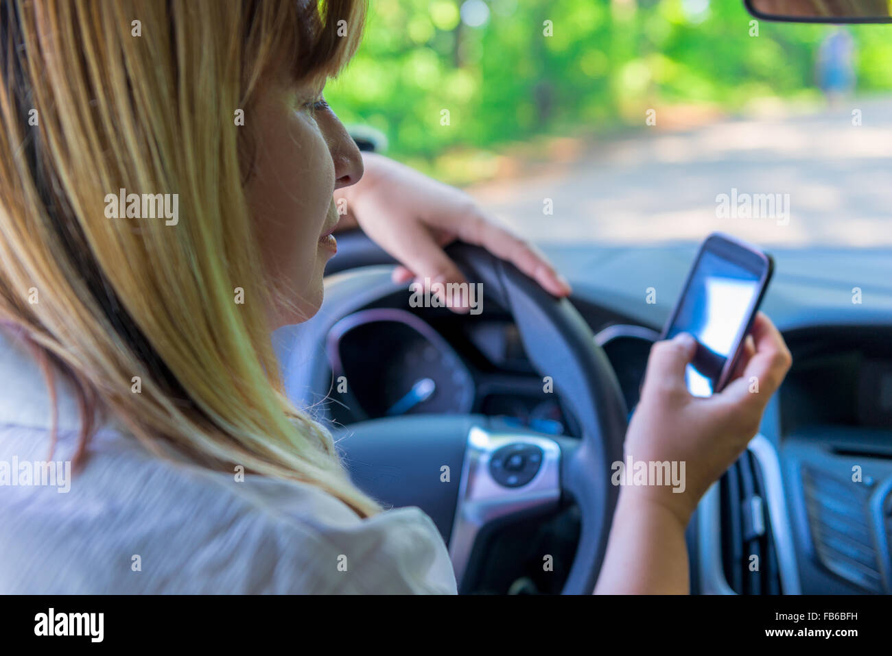 Donna che guarda il telefono alla guida di una macchina Foto Stock