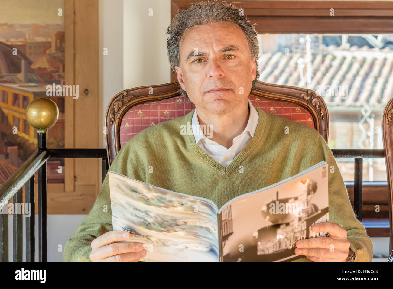 Caucasian uomo di mezza età leggendo una rivista comodamente seduti in un salotto vintage e sembra confusa e domande Foto Stock