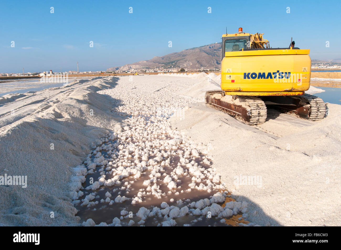 L'Italia, Sicilia, Trapani. La Komatsu escavatore cingolato di raccolta del sale del mare da un laghetto di evaporazione. Foto Stock