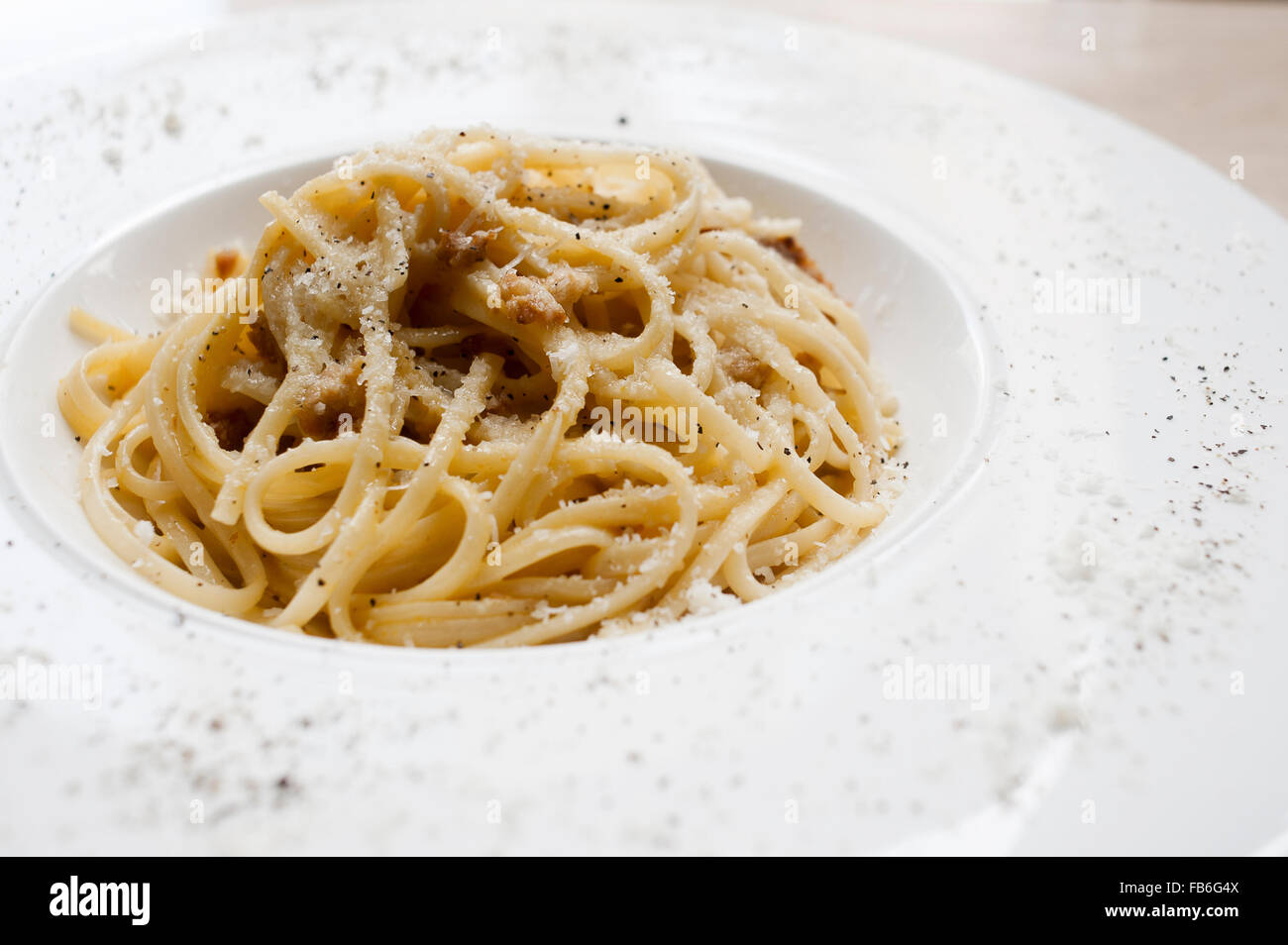 Spaghetti alla carbonara con pepe nero e parmigiano, presentato su un piatto bianco in un ristorante italiano. Foto Stock