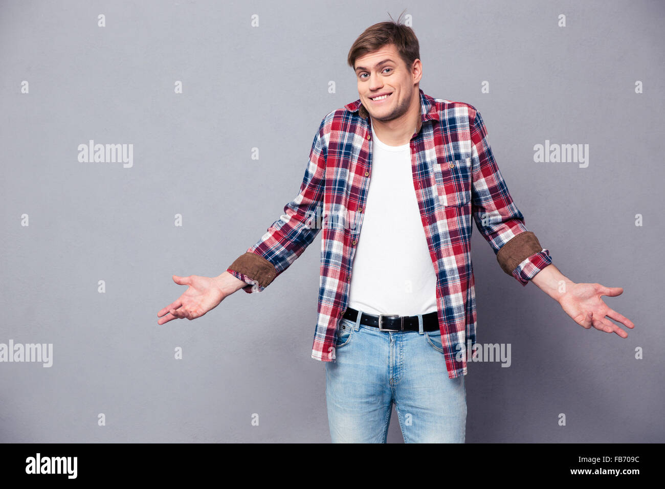 Confuso carino giovane uomo in plaid shirt e jeans in piedi e scrollare su sfondo grigio Foto Stock