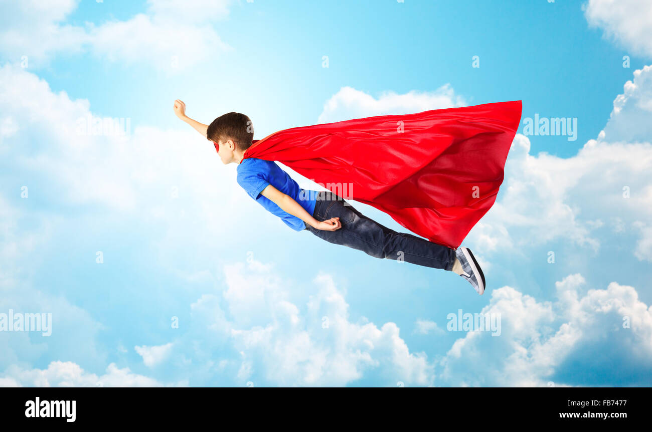 Ragazzo in rosso superhero cape e maschera e volare in aria Foto Stock