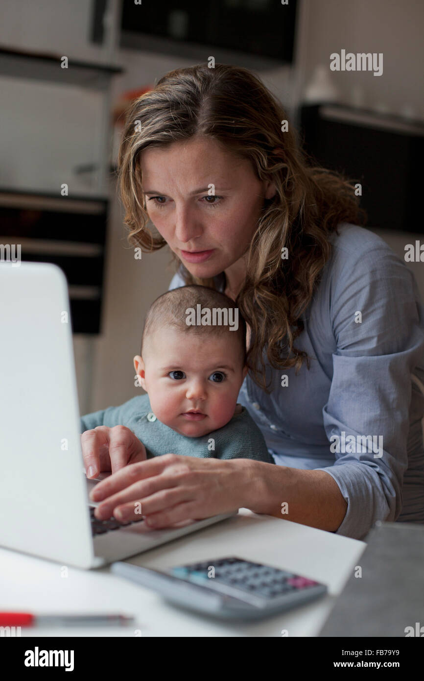 Donna al lavoro su computer portatile mentre è seduto con la bambina a casa Foto Stock