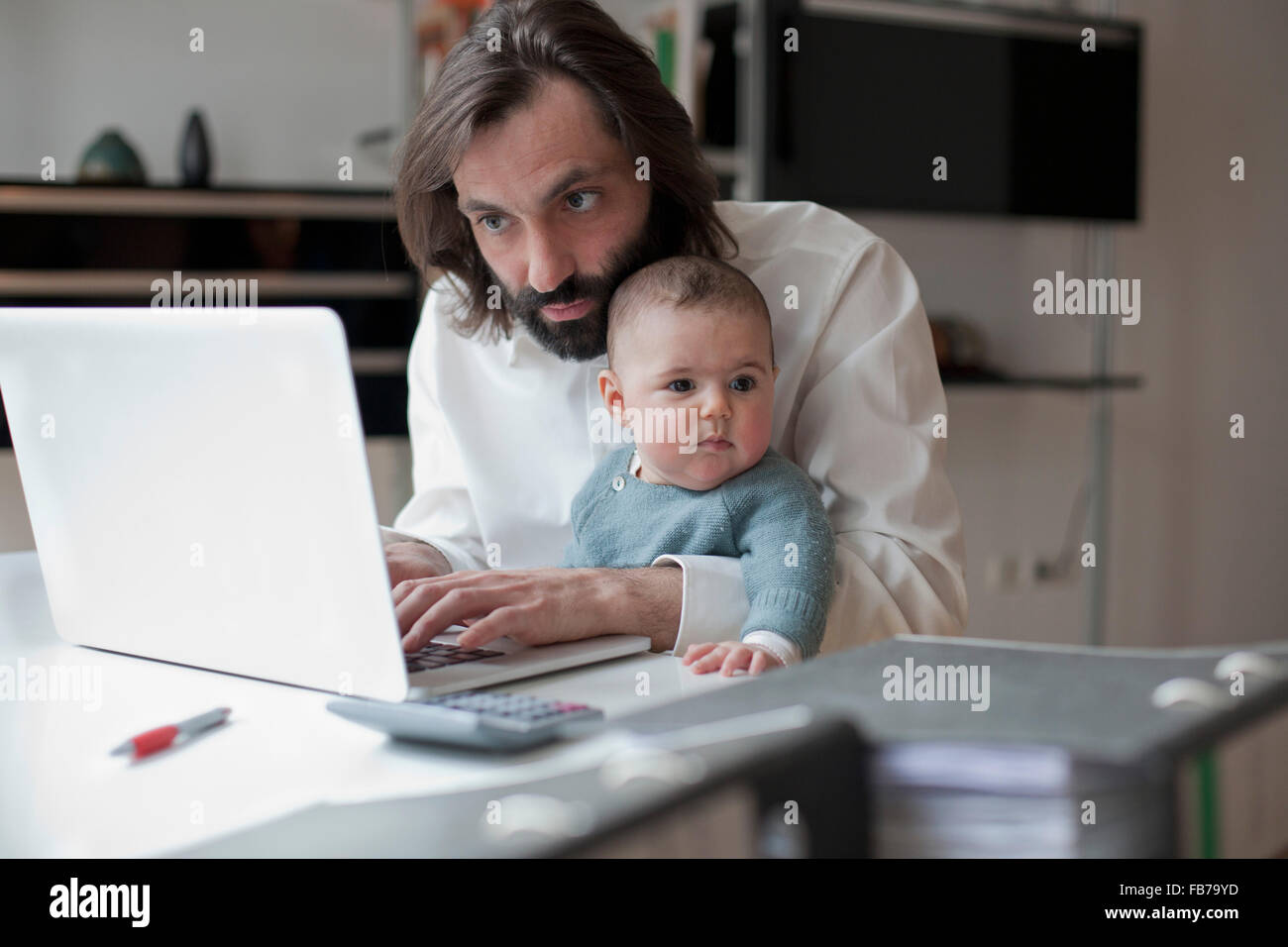Metà uomo adulto lavorando sul computer portatile mentre è seduto con la bambina a casa Foto Stock