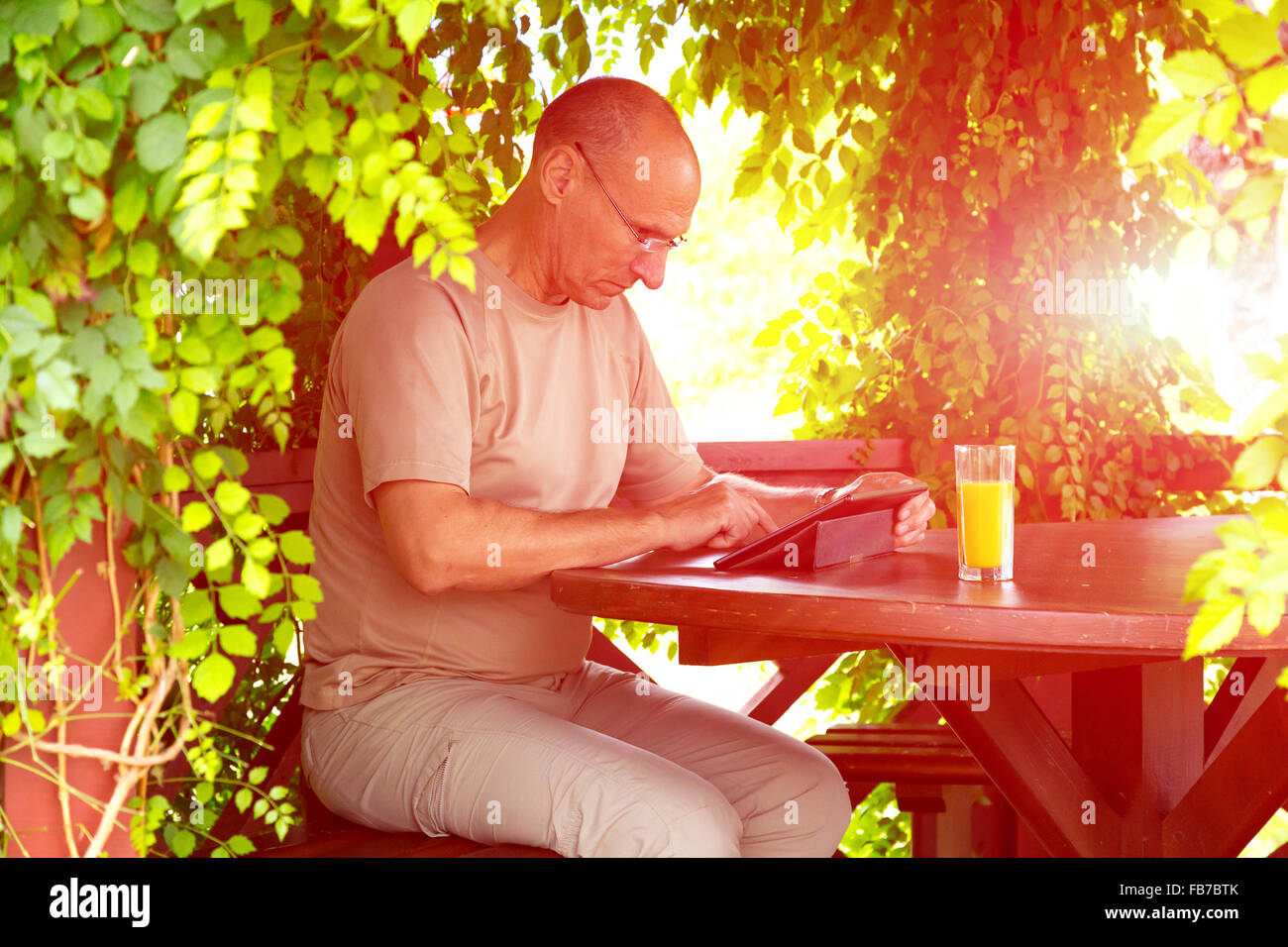 Vestiti Casual Uomo con gadget e un bicchiere di succo di arancia seduta in legno arbor Foto Stock