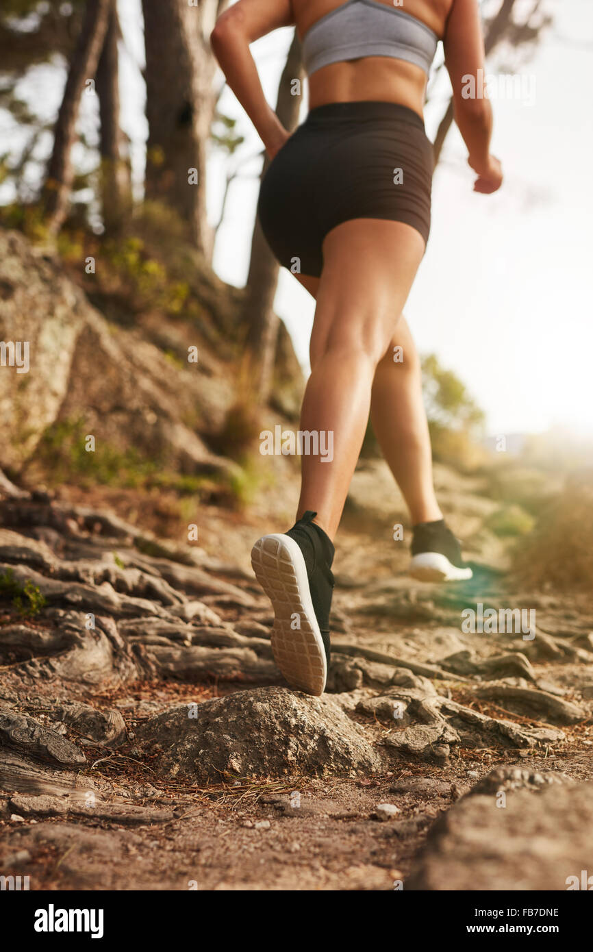 La donna in esecuzione su sentieri rocciosi sul versante della collina. Vista posteriore di immagine femminile la formazione all'esterno. Foto Stock