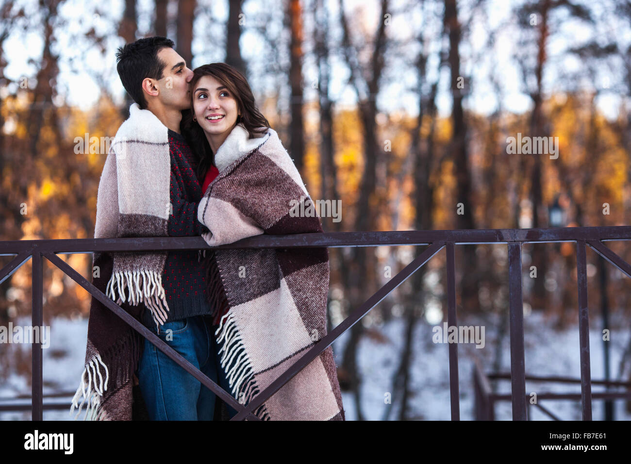 Giovane uomo baciare donna avvolto in un lenzuolo sul ponte durante il periodo invernale Foto Stock