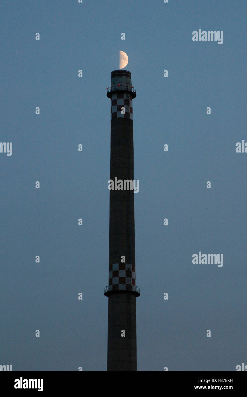 Basso angolo vista della pila di fumo e mezza luna contro il cielo blu al tramonto Foto Stock