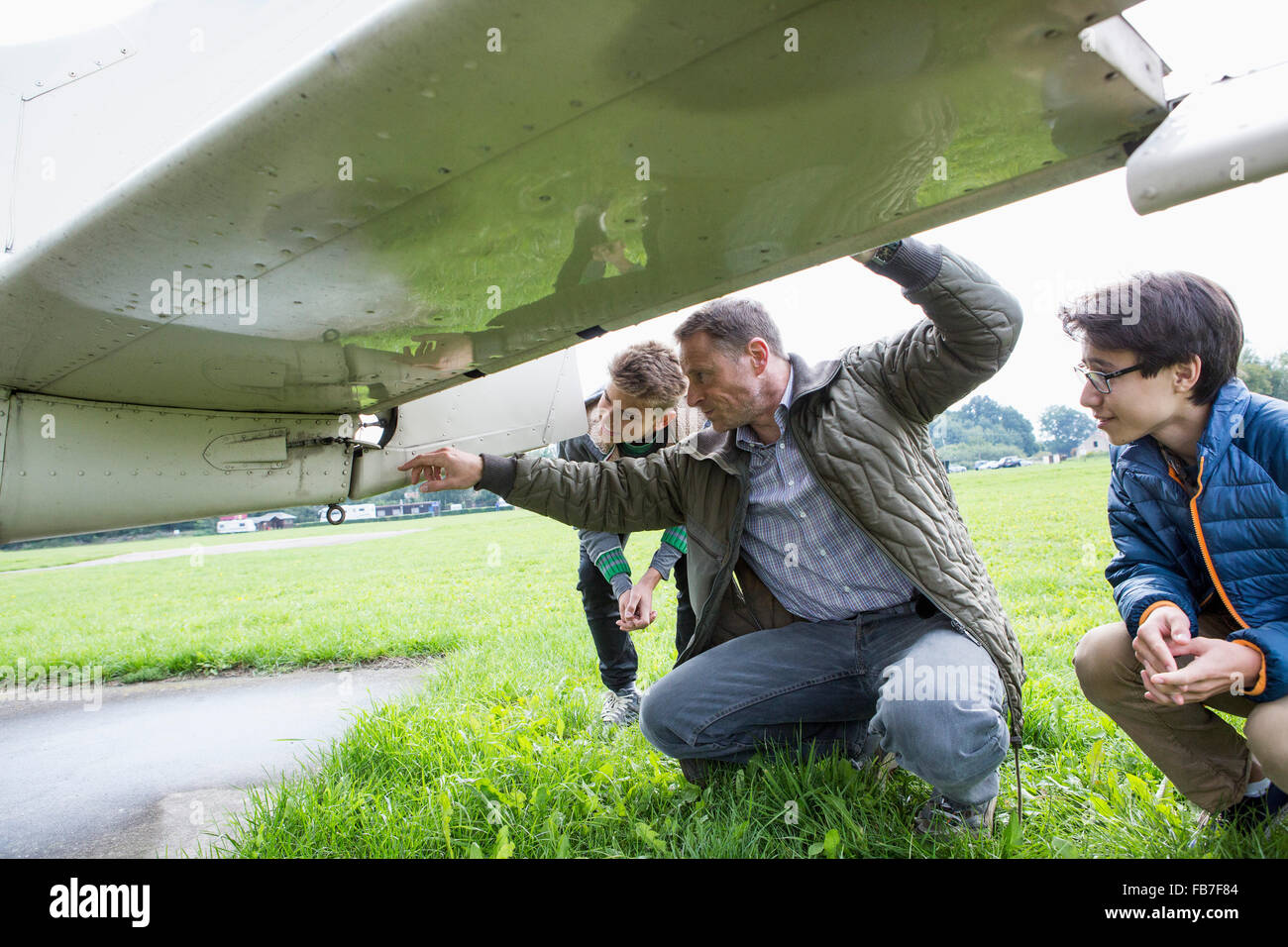 Padre spiegando parti di aereo a figli sul campo Foto Stock
