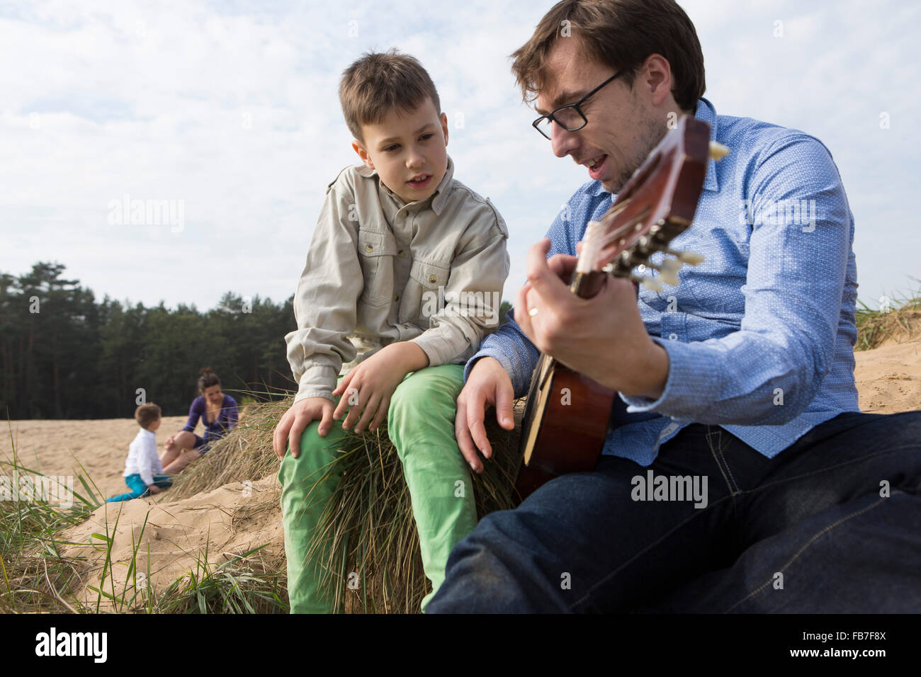 Ragazzo che guarda al padre a suonare la chitarra sul campo Foto Stock