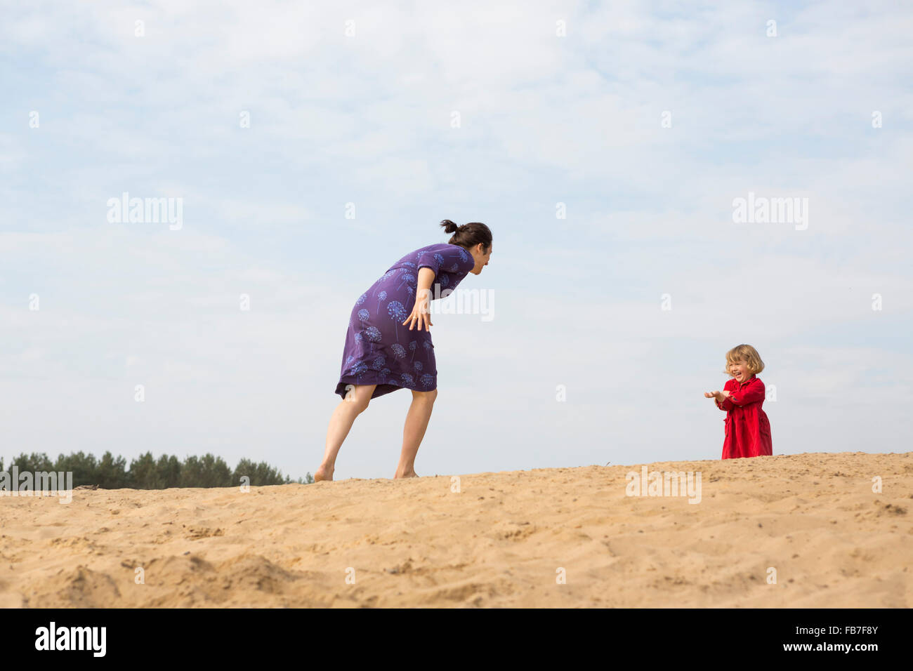 Madre e figlia giocando sulla sabbia contro sky Foto Stock