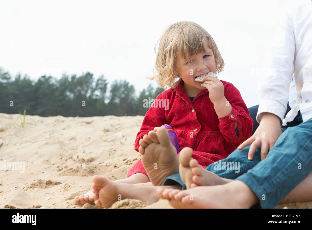 Ritratto di ragazza carina mangiando snack seduti con la famiglia sulla sabbia Foto Stock