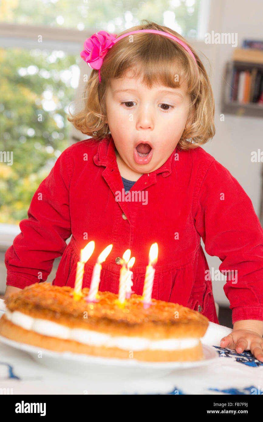 Ragazza carina soffiando candeline di compleanno a tavola Foto Stock