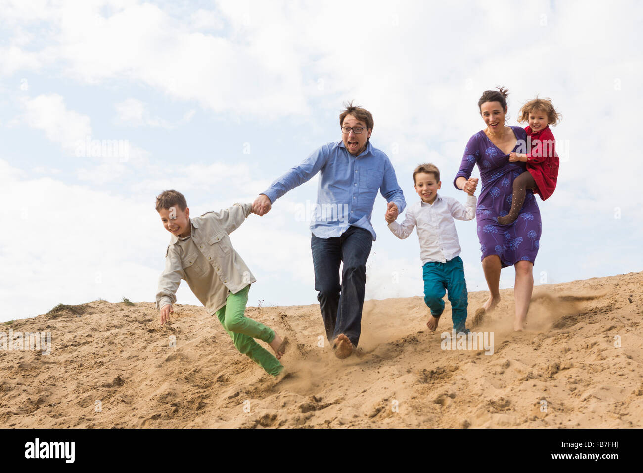 Famiglia allegra tenendo le mani mentre è in esecuzione sulla duna di sabbia contro sky Foto Stock