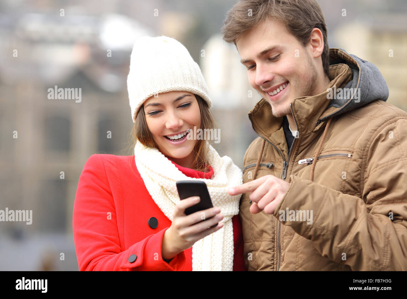 Coppia felice consultazione uno smart phone in inverno in strada Foto Stock