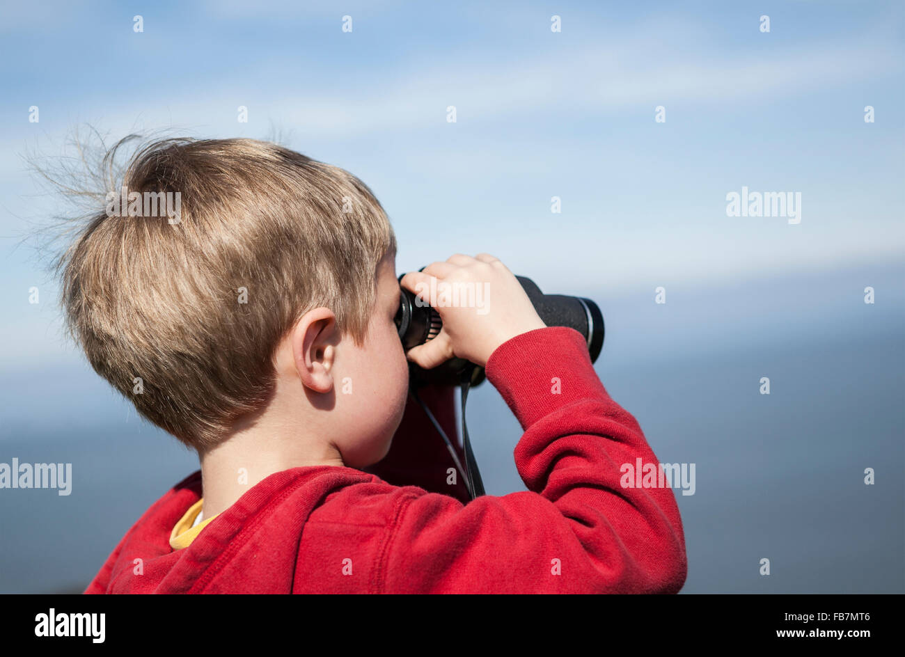 Ragazzo giovane che si affaccia al mare con un binocolo Foto Stock