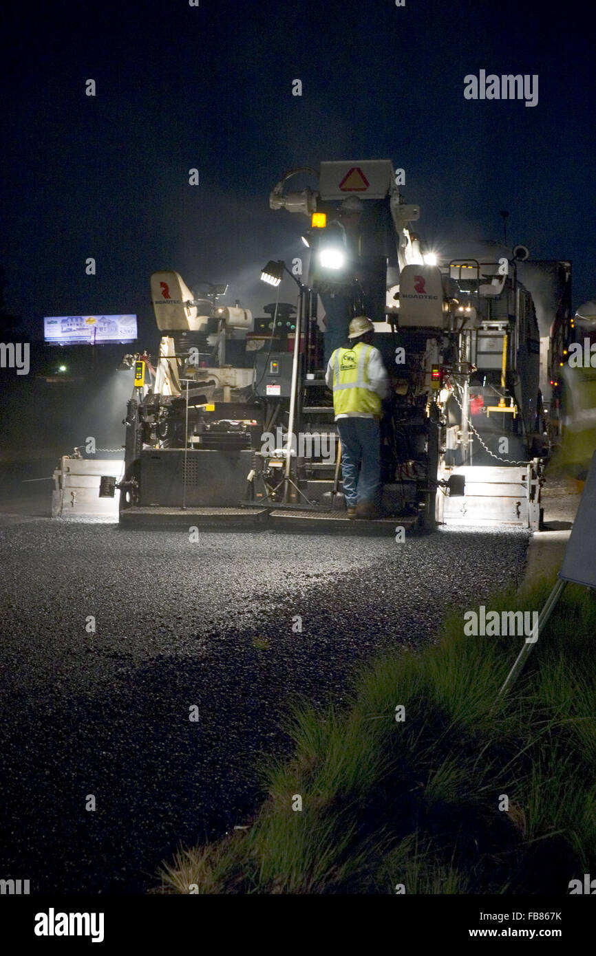 I lavoratori di sostare dietro un asfalto spandiconcime immissione hot mix durante la strada interstatale di lavorare di notte. Foto Stock