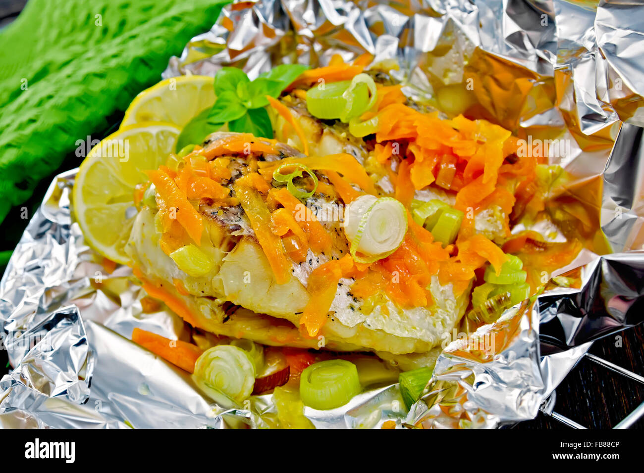 Luccio con carote, porro, il basilico e le fette di limone in una lamina su una griglia di metallo, asciugamano verde sullo sfondo dei pannelli in legno Foto Stock