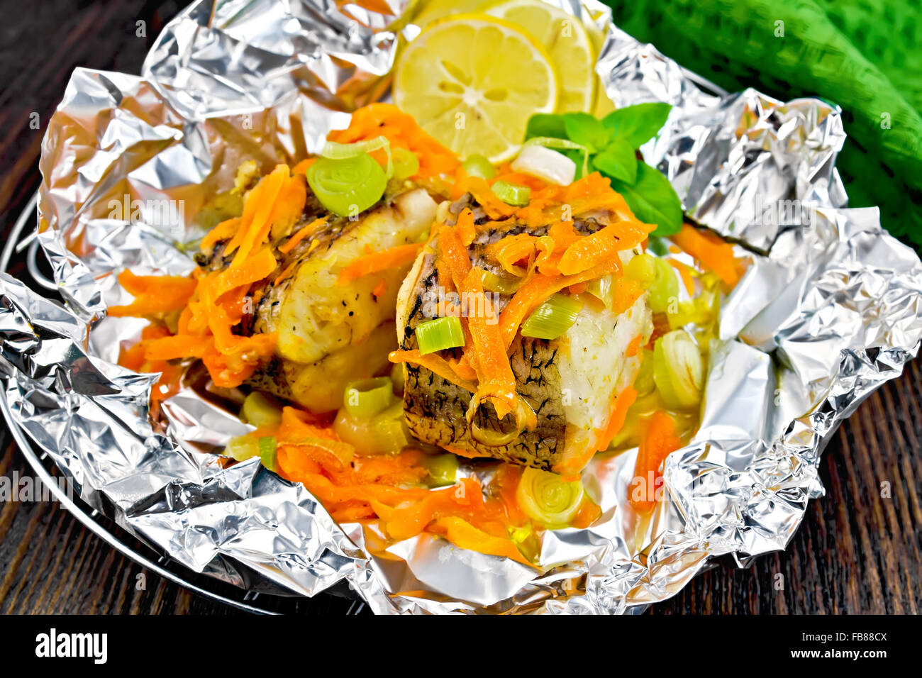 Luccio con carote, porro, il basilico e le fette di limone sulla griglia in lamina, un asciugamano verde su tavole di legno sfondo Foto Stock