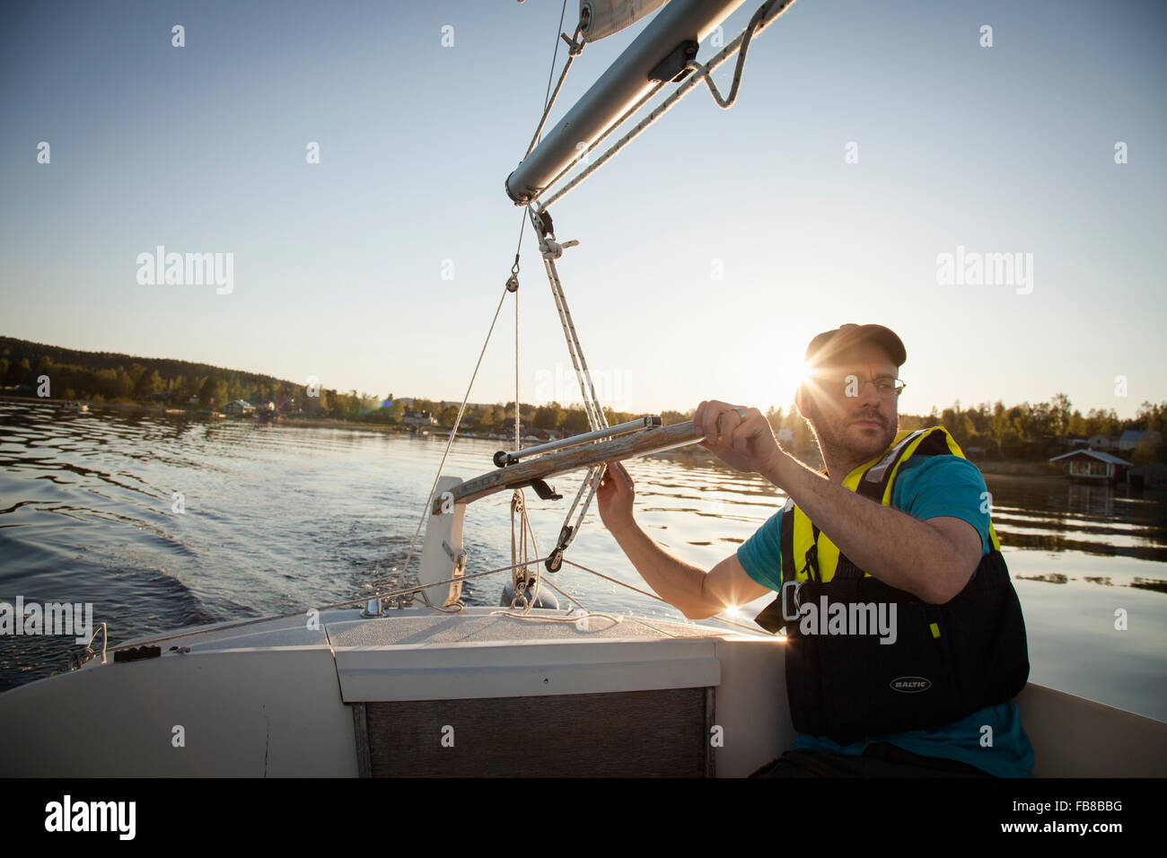 La Svezia, Medelpad, Juniskar, uomo maturo barca a vela al tramonto Foto Stock