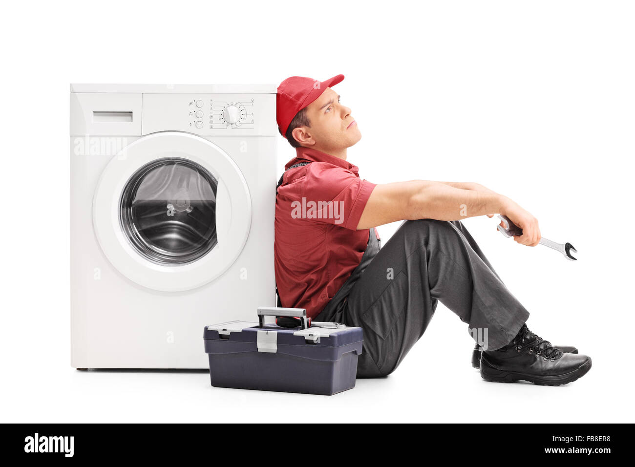 Studio shot di un triste plumber seduto a terra da una macchina di lavaggio e di pensiero isolato su sfondo bianco Foto Stock