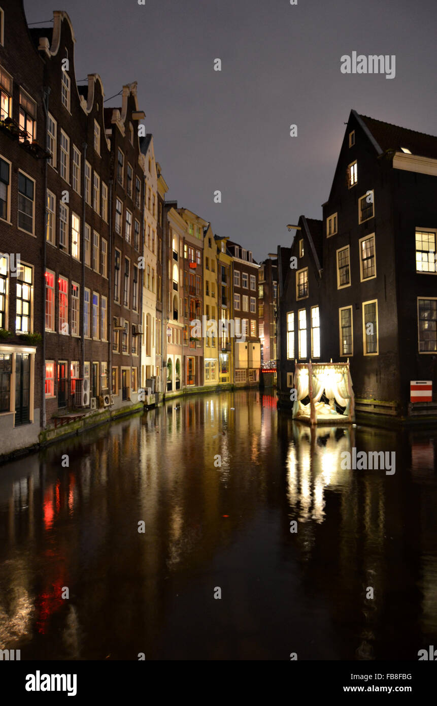 Case a schiera e arte di installazione lungo la Oudezijds Achterburgwal di notte, Amsterdam, Paesi Bassi Foto Stock