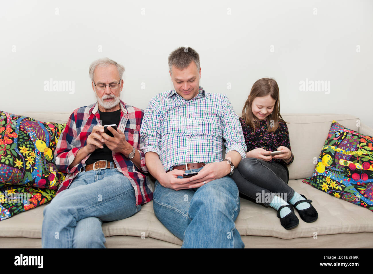 La ragazza (8-9) texting con la famiglia sul divano Foto Stock