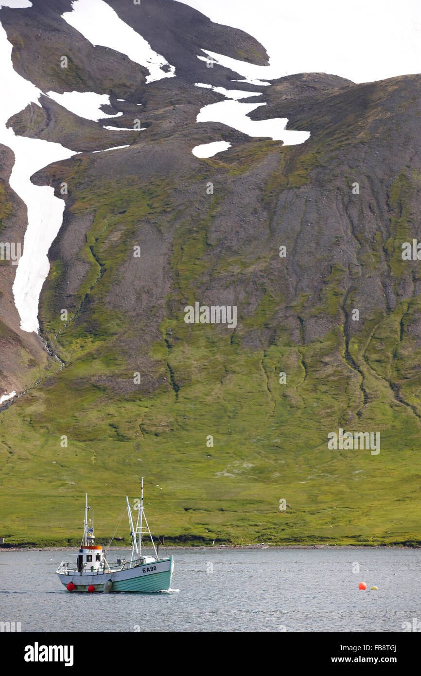 Barca da pesca contro big mountain in background nel fiordo di Siglufjörður Affitto Islanda Foto Stock