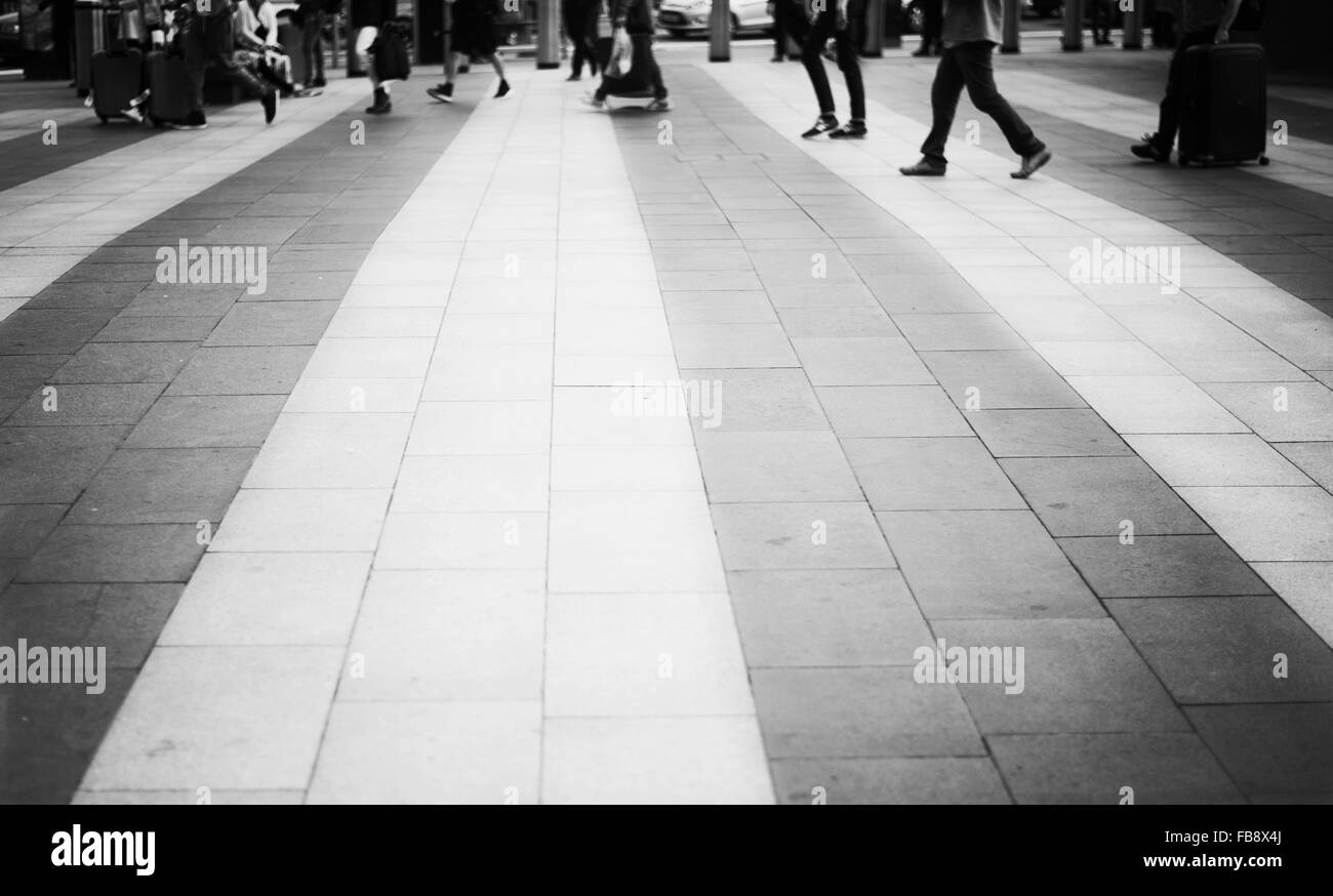 Zebra pedonale di attraversamento al di fuori alla stazione ferroviaria di Kings Cross a Londra. In bianco e nero dei piedi e delle gambe in background. Foto Stock