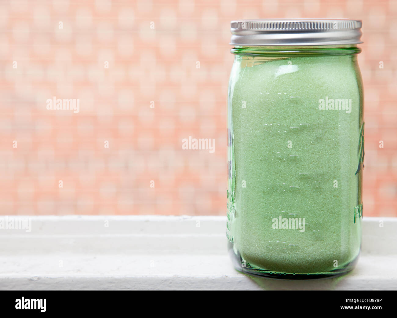 Organici di granulati di zucchero di canna di vetro verde laureato mason jar, sul davanzale con sfondo mattone. Foto Stock